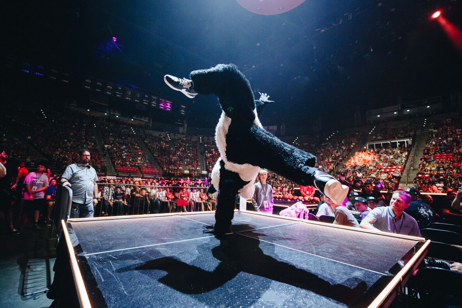 A performer mid-flip on an arena stage, crowd lit in red behind him